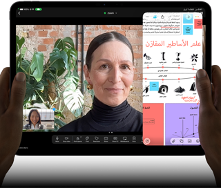جهاز iPad Pro، الجزء الأمامي الخارجي، الوضع الأفقي، لون أسود فلكي، زوايا مدورة، إطار شاشة أسود، يدان تحملان الجهاز من الجانب الأيسر والأيمن، شاشة تعرض محادثة عبر فيس تايم تتم ترجمتها مباشرة، وتطبيق تعليمي يُظهر عرضاً تقديمياً بعنوان 'علم الأساطير المقارَن' مع نصوص ومخططات وملاحظات مكتوبة بخط اليد