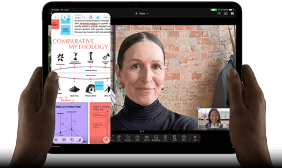 iPad Pro, front exterior, landscape orientation, space black color, rounded corners, black display bezel, hands holding left and right sides, display showing a FaceTime conversation being live translated, and an educational app showing a presentation of "Comparative Mythology" with text, diagrams, and handwritten notes