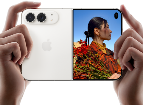 جهاز iPhone Duo، لون أبيض النجوم، يدان تحملان الجهاز في الوضع الأفقي، مفتوح، اللوحة اليسرى تعرض الكاميرا المزدوجة 48MP Fusion الخلفية، اللوحة اليمنى تعرض شخصاً تُلتقط صورته على الشاشة الخارجية، يمكن لهذا الشخص رؤية وجهه لأن الصورة تُلتقط باستخدام ميزة Duo Preview‏