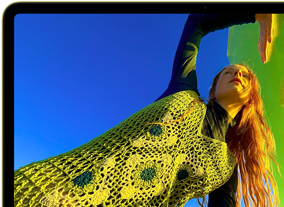 MacBook Neo, citrus color, screen shows a smiling person lying in a sunny field of flowers